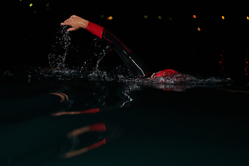 Image showing A determined professional triathlete undergoes rigorous night time training in cold waters, showcasing dedication and resilience in preparation for an upcoming triathlon swim competition