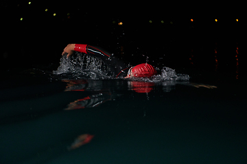 Image showing A determined professional triathlete undergoes rigorous night time training in cold waters, showcasing dedication and resilience in preparation for an upcoming triathlon swim competition