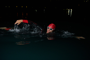 Image showing A determined professional triathlete undergoes rigorous night time training in cold waters, showcasing dedication and resilience in preparation for an upcoming triathlon swim competition