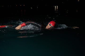 Image showing A determined professional triathlete undergoes rigorous night time training in cold waters, showcasing dedication and resilience in preparation for an upcoming triathlon swim competition