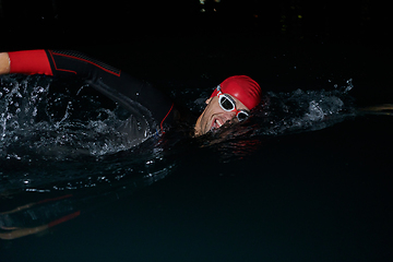 Image showing A determined professional triathlete undergoes rigorous night time training in cold waters, showcasing dedication and resilience in preparation for an upcoming triathlon swim competition