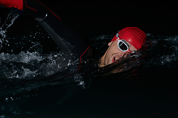 Image showing A determined professional triathlete undergoes rigorous night time training in cold waters, showcasing dedication and resilience in preparation for an upcoming triathlon swim competition