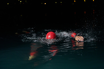 Image showing A determined professional triathlete undergoes rigorous night time training in cold waters, showcasing dedication and resilience in preparation for an upcoming triathlon swim competition