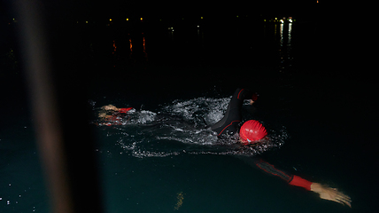 Image showing A determined professional triathlete undergoes rigorous night time training in cold waters, showcasing dedication and resilience in preparation for an upcoming triathlon swim competition