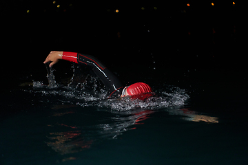 Image showing A determined professional triathlete undergoes rigorous night time training in cold waters, showcasing dedication and resilience in preparation for an upcoming triathlon swim competition