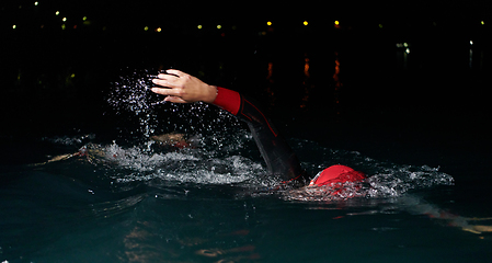 Image showing A determined professional triathlete undergoes rigorous night time training in cold waters, showcasing dedication and resilience in preparation for an upcoming triathlon swim competition