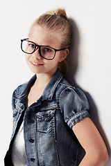 Image showing Child, portrait and smiling with glasses in studio, cool and confidence by white background. Female person, girl and casual clothing or style by backdrop, kid and denim jacket pride for eyesight test