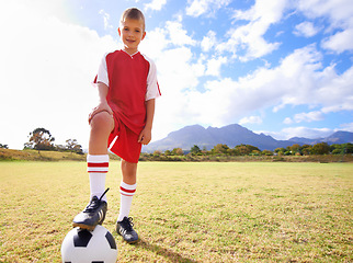 Image showing Happy child, soccer ball and sports on green grass for training or practice with clouds and blue sky. Portrait of young football player smile ready for kick off game, match or outdoor field in nature