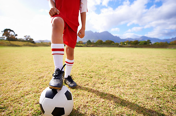 Image showing Child, soccer ball and legs on green grass for sports, training or practice with clouds and blue sky. Closeup of football player with foot ready for kick off, game or match on outdoor field in nature