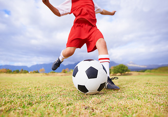 Image showing Child, kicking and soccer ball on green grass for sports, training or practice with clouds and blue sky. Closeup of football player foot ready for kick off, game or match on outdoor field in nature