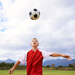 Image showing Child, soccer ball and playing on green grass for sports, training or practice with clouds and blue sky. Young football player or athlete ready for kick off, game or match on outdoor field in nature