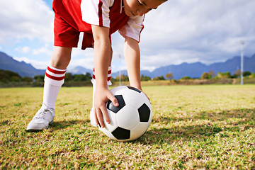 Image showing Child, hands and soccer ball for sports on green grass in training or practice with clouds and blue sky. Closeup of young football player ready for kick off game or match on outdoor field in nature