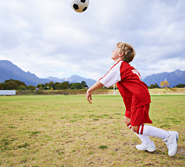 Image showing Boy, soccer ball and playing on green grass for sports, training or practice with clouds and blue sky. Young football player, child or kid ready for kick off, game or match on outdoor field in nature