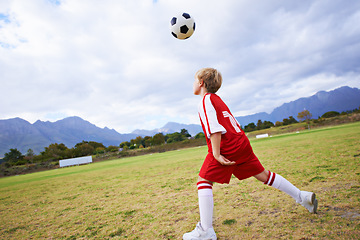 Image showing Kid, soccer ball and playing on green grass for sports, training or practice with clouds and blue sky. Young football player or athlete ready for kick off, game or match on outdoor field in nature