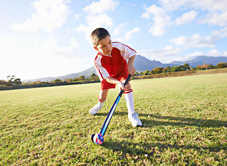 Image showing Child, ball and playing hockey on green grass for game, sports or outdoor practice match. Young kid or player enjoying day on field for fitness, activity or training alone in nature with blue sky