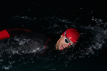 Image showing A determined professional triathlete undergoes rigorous night time training in cold waters, showcasing dedication and resilience in preparation for an upcoming triathlon swim competition