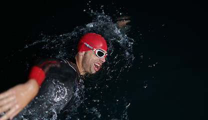 Image showing A determined professional triathlete undergoes rigorous night time training in cold waters, showcasing dedication and resilience in preparation for an upcoming triathlon swim competition