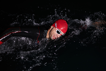 Image showing A determined professional triathlete undergoes rigorous night time training in cold waters, showcasing dedication and resilience in preparation for an upcoming triathlon swim competition