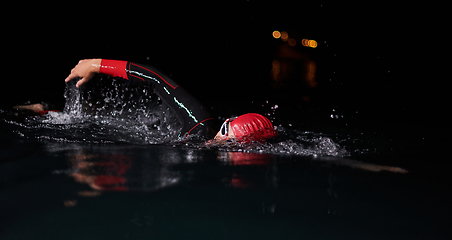 Image showing A determined professional triathlete undergoes rigorous night time training in cold waters, showcasing dedication and resilience in preparation for an upcoming triathlon swim competition