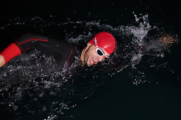 Image showing A determined professional triathlete undergoes rigorous night time training in cold waters, showcasing dedication and resilience in preparation for an upcoming triathlon swim competition