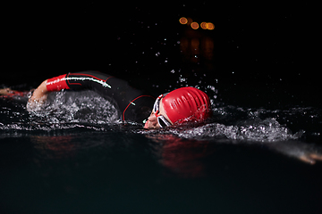 Image showing A determined professional triathlete undergoes rigorous night time training in cold waters, showcasing dedication and resilience in preparation for an upcoming triathlon swim competition