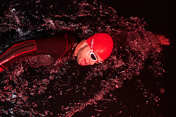 Image showing A determined professional triathlete undergoes rigorous night time training in cold waters, showcasing dedication and resilience in preparation for an upcoming triathlon swim competition