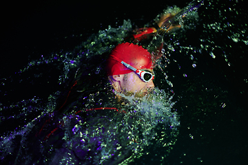 Image showing Authentic triathlete swimmer having a break during hard training on night neon gel light