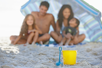 Image showing Big family, sand and box on beach with umbrella, spade or bucket for playing on ocean coast. Blue and yellow toys on sandy shore with people for fun bonding, relax or outdoor holiday weekend together