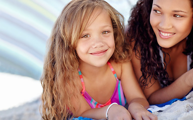 Image showing Happy girl, portrait and relax on beach with mother for fun day outside by the ocean coast in nature. Face of little female person, child or kid smile lying on sand by sea with mom for family bonding