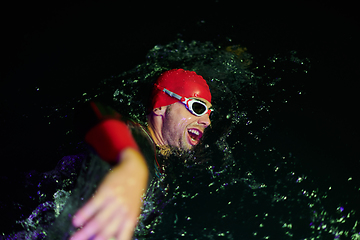 Image showing Authentic triathlete swimmer having a break during hard training on night neon gel light