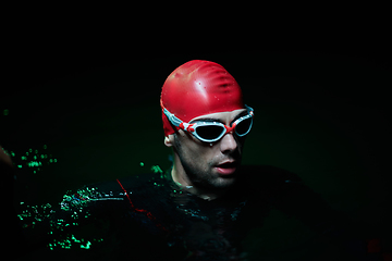 Image showing Authentic triathlete swimmer having a break during hard training on night neon gel light