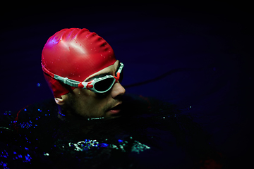 Image showing Authentic triathlete swimmer having a break during hard training on night neon gel light