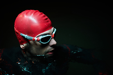 Image showing Authentic triathlete swimmer having a break during hard training on night neon gel light