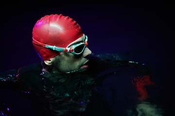 Image showing Authentic triathlete swimmer having a break during hard training on night neon gel light