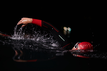 Image showing A determined professional triathlete undergoes rigorous night time training in cold waters, showcasing dedication and resilience in preparation for an upcoming triathlon swim competition