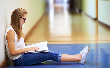 Image showing Woman, teenager and student reading book in hallway at school for learning, education or studying. Female person or young child or kid sitting on floor in corridor with textbook outside classroom