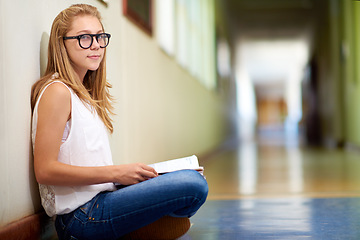 Image showing Happy woman, teenager and student with book in hallway at school for learning, education or studying. Portrait of female person or young child sitting on floor in corridor with textbook by classroom