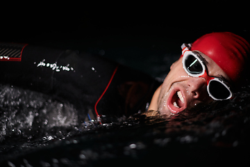 Image showing A determined professional triathlete undergoes rigorous night time training in cold waters, showcasing dedication and resilience in preparation for an upcoming triathlon swim competition