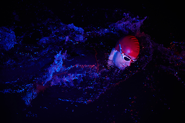 Image showing Authentic triathlete swimmer having a break during hard training on night neon gel light