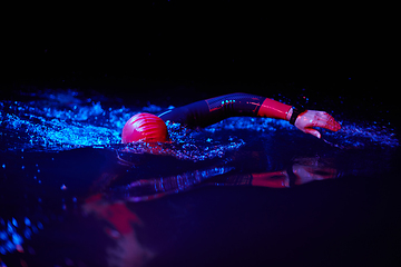 Image showing Authentic triathlete swimmer having a break during hard training on night neon gel light