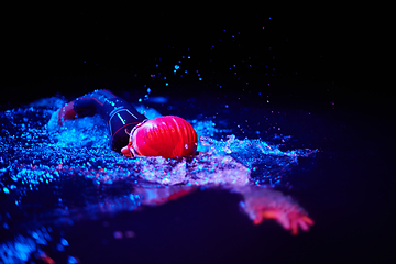 Image showing Authentic triathlete swimmer having a break during hard training on night neon gel light