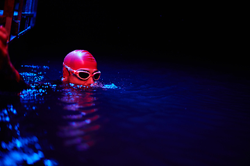 Image showing Authentic triathlete swimmer having a break during hard training on night neon gel light