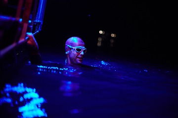 Image showing authentic triathlete swimmer having a break during hard training on night neon gel light