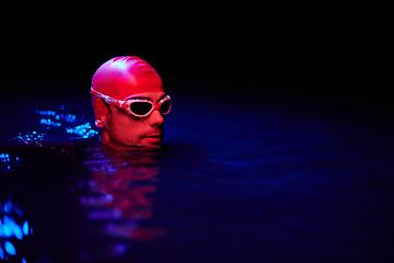 Image showing Authentic triathlete swimmer having a break during hard training on night neon gel light