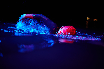 Image showing Authentic triathlete swimmer having a break during hard training on night neon gel light