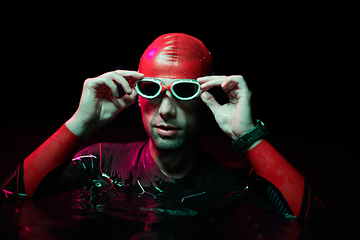 Image showing Authentic triathlete swimmer having a break during hard training on night neon gel light