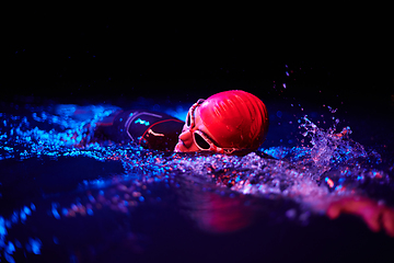 Image showing Authentic triathlete swimmer having a break during hard training on night neon gel light