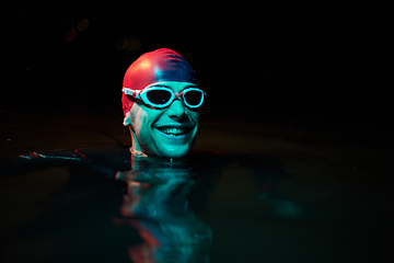 Image showing Authentic triathlete swimmer having a break during hard training on night neon gel light