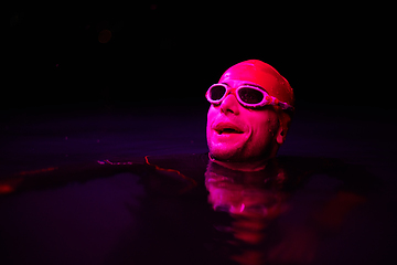 Image showing Authentic triathlete swimmer having a break during hard training on night neon gel light