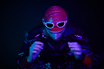 Image showing authentic triathlete swimmer having a break during hard training on night neon gel light